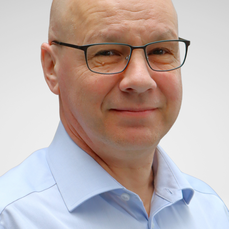 Silmälasipäinen mies kauluspaidassa katsoo kameraan.