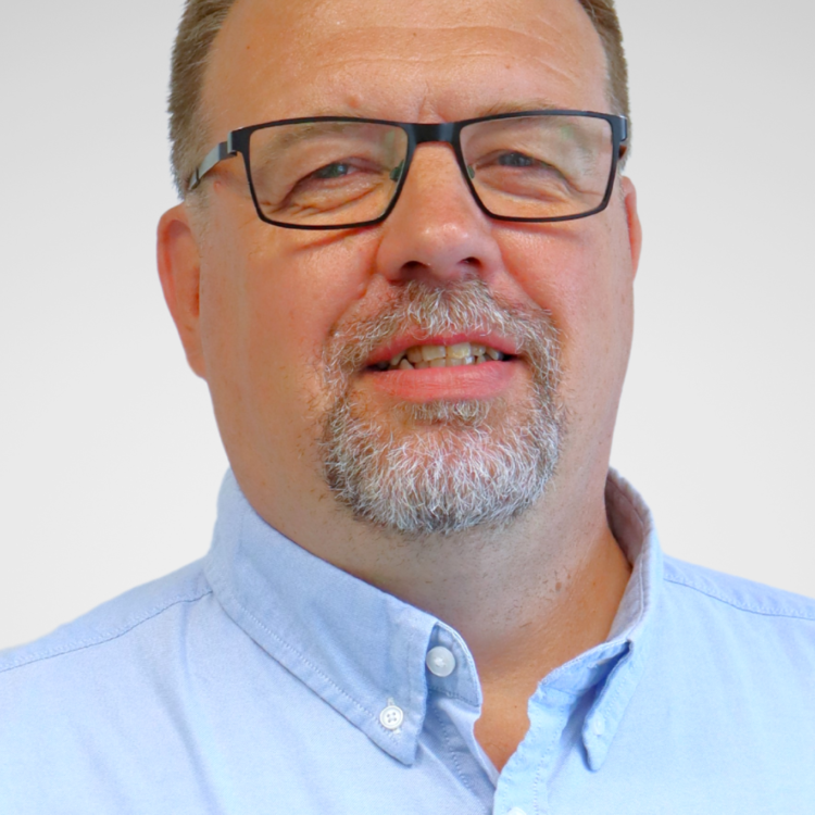A man wearing glasses looking at the camera and smiling.
